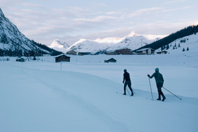 Zwei Langläufer genießen die verschneite Landschaft in Lech/Zürs am Arlberg, umgeben von majestätischen Bergen.