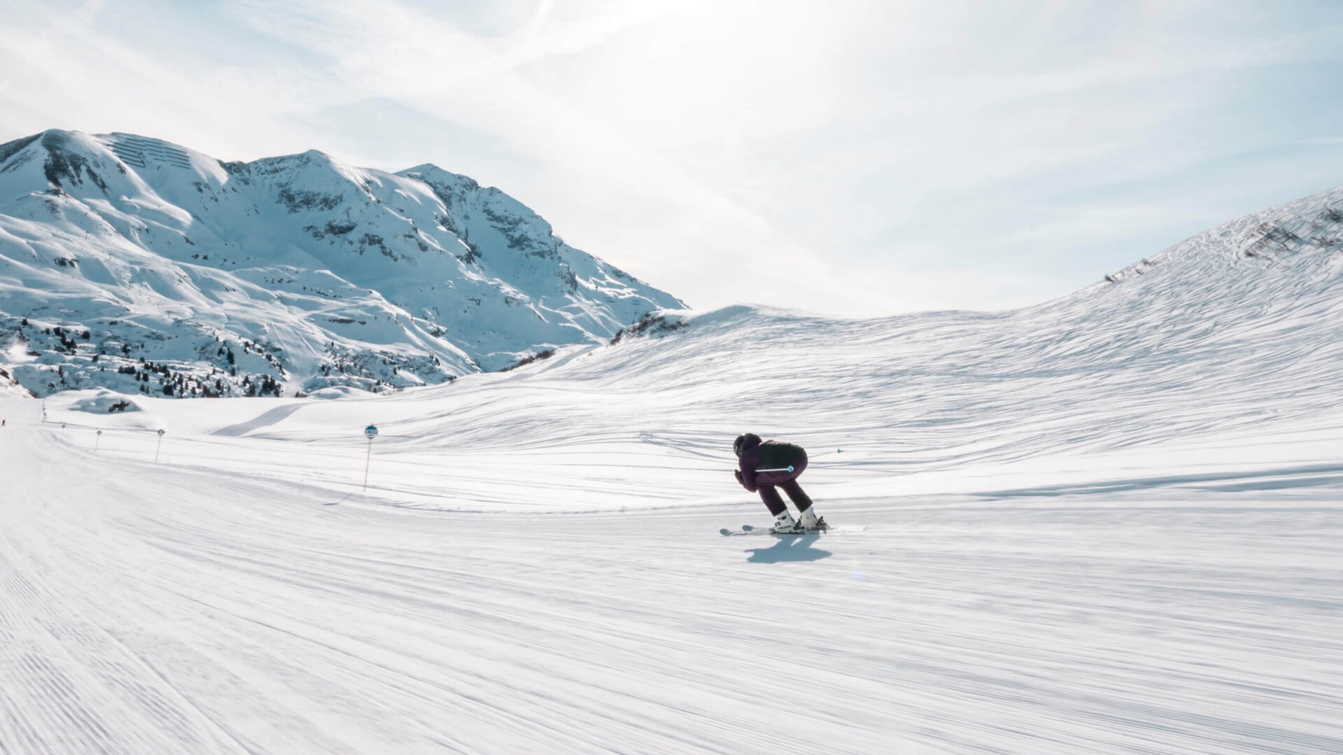 Skifahrer auf einer sonnigen Piste in Lech/Zürs, umgeben von schneebedeckten Bergen und makellosem Himmel.