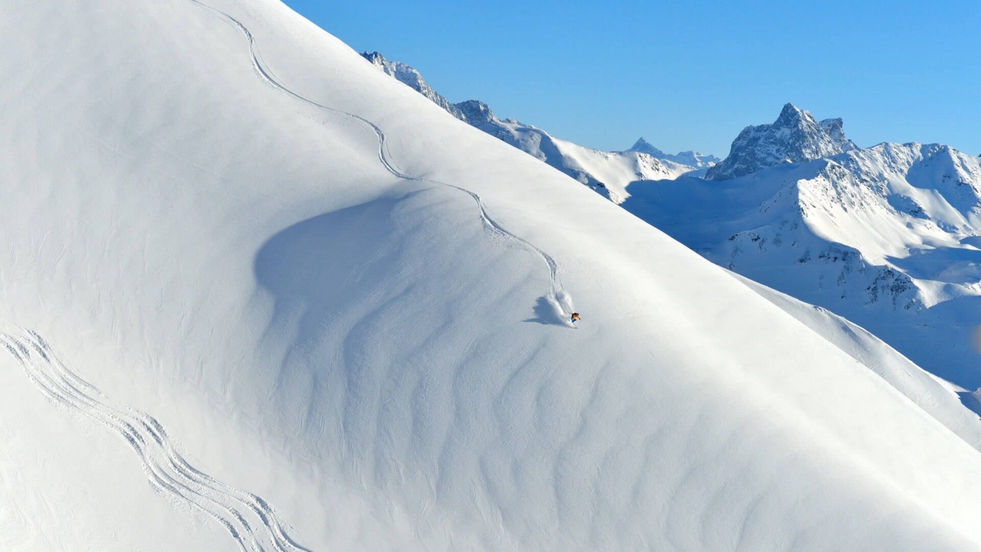 Ein Skifahrer gleitet durch frischen Pulverschnee in den Alpen von Lech/Zürs am Arlberg unter klarem Himmel.