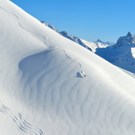 Ein Skifahrer gleitet durch frischen Pulverschnee in den Alpen von Lech/Zürs am Arlberg unter klarem Himmel.