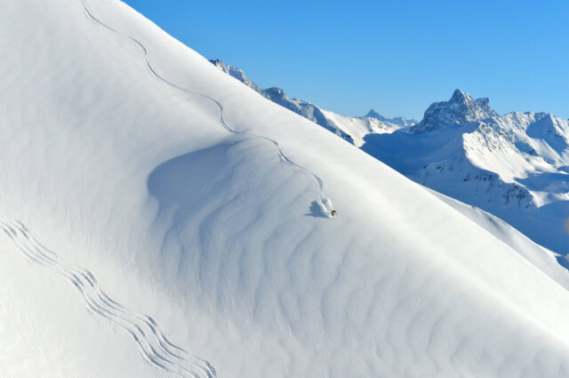 Ein Skifahrer gleitet durch frischen Pulverschnee in den Alpen von Lech/Zürs am Arlberg unter klarem Himmel.