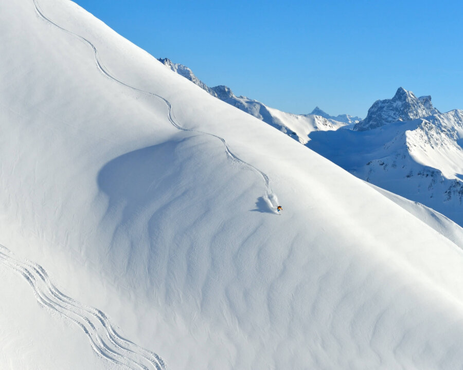 Ein Skifahrer gleitet durch frischen Pulverschnee in den Alpen von Lech/Zürs am Arlberg unter klarem Himmel.