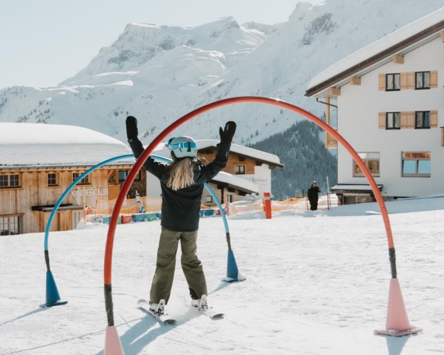 Ein Skifahrer durchläuft bunte Tore im Schnee, mit majestätischen Bergen und dem Hotel Edelweiss im Hintergrund.