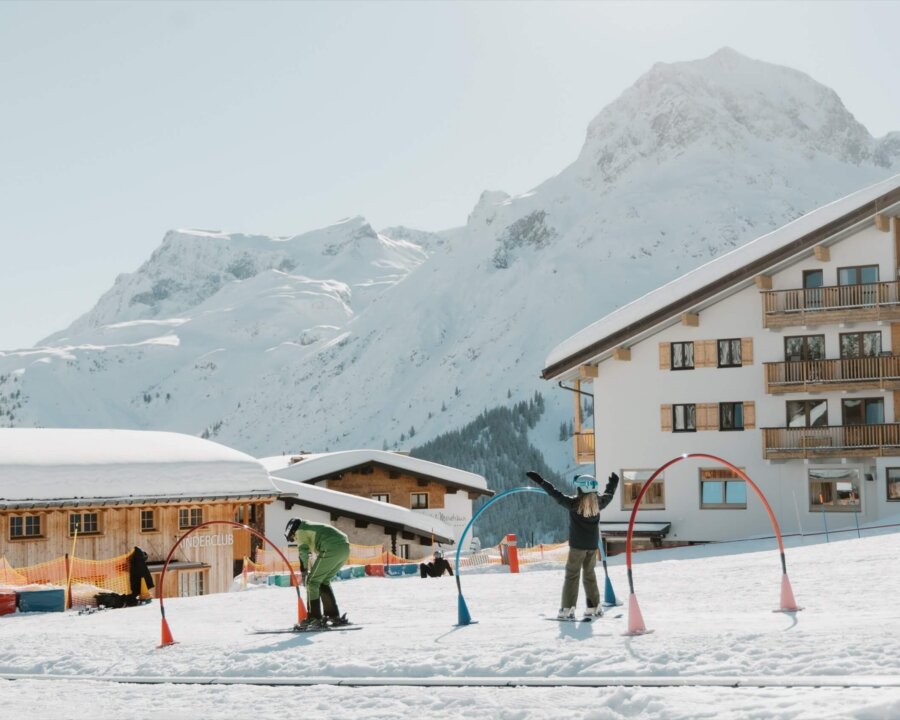 Skifahrer im Schnee vor dem Hotel Edelweiss in Lech/Zürs am Arlberg, mit malerischer Bergkulisse.
