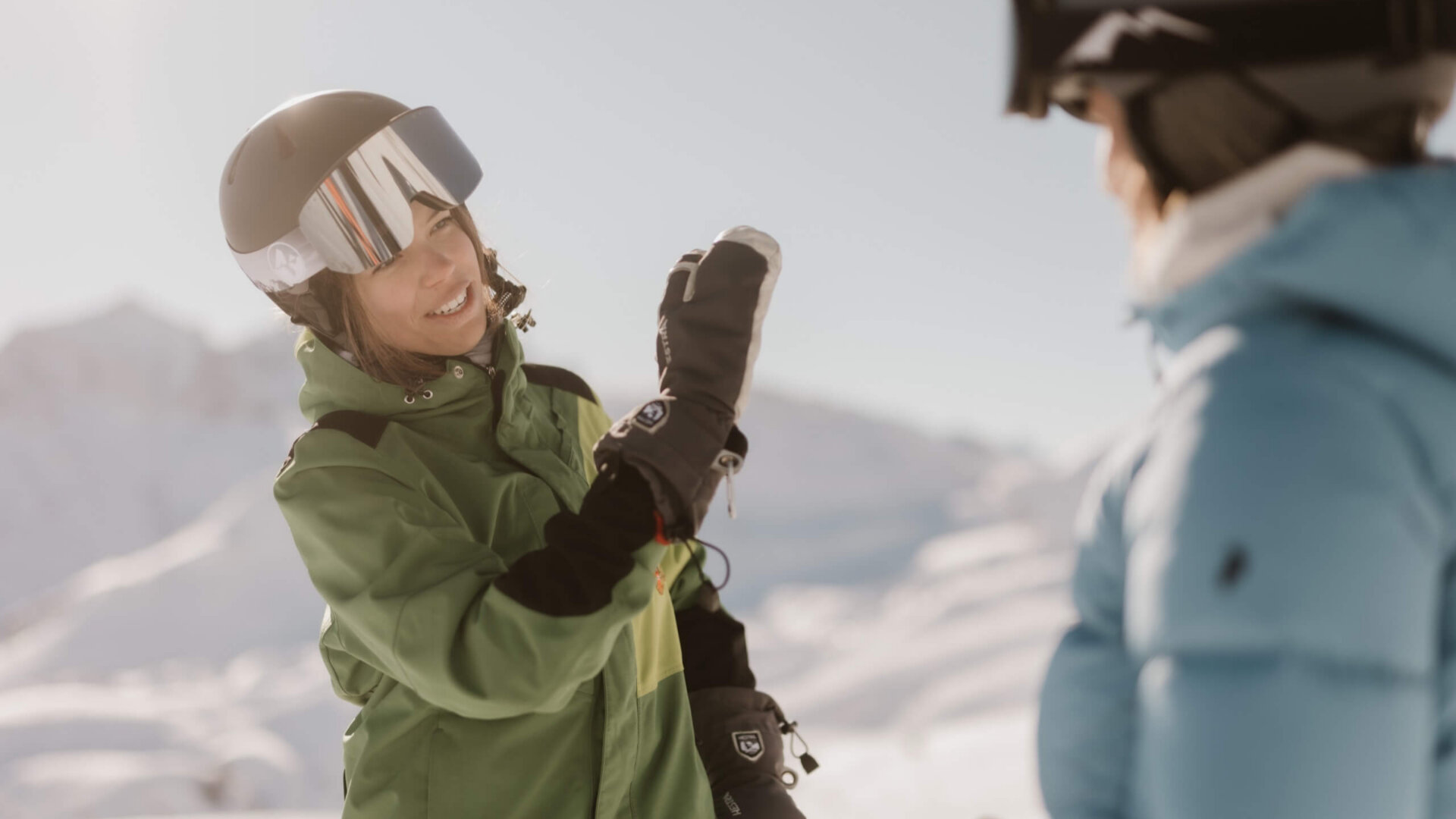 Zwei Frauen im grünen und blauen Skianzug genießen den sonnigen Tag im Schnee in Lech/Zürs. Perfect for winter adventures!