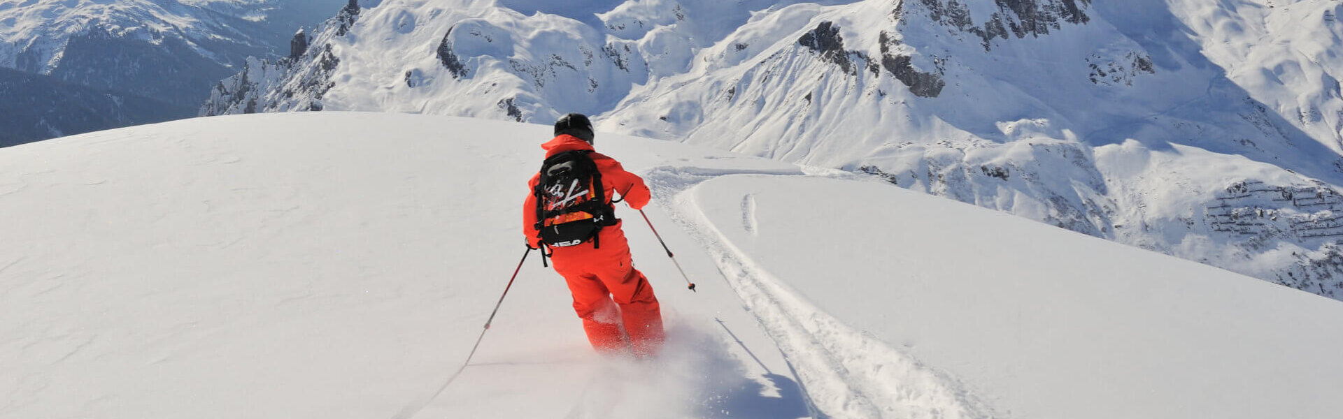 Skifahrer in orangefarbenem Anzug gleitet über frischen Schnee in den majestätischen Alpen rund um Lech/Zürs.