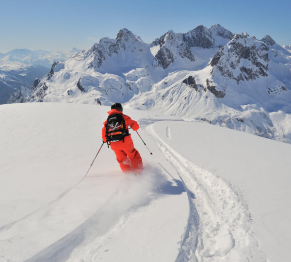 Skifahrer in orangefarbenem Anzug gleitet über frischen Schnee in den majestätischen Alpen rund um Lech/Zürs.