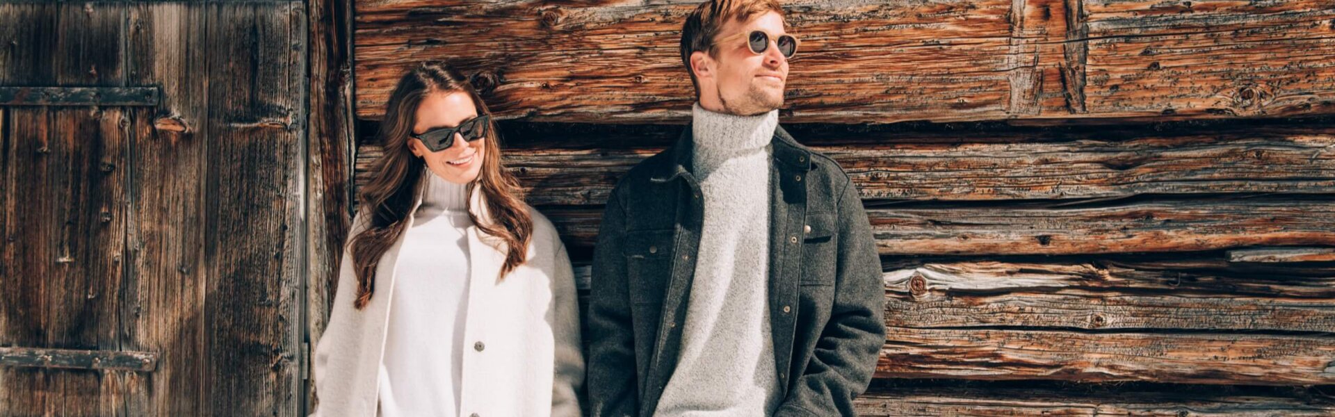 Paar in stylischer Winterkleidung vor einer Holzfassade, ideal für romantische Urlaubsaufnahmen in Lech/Zürs.
