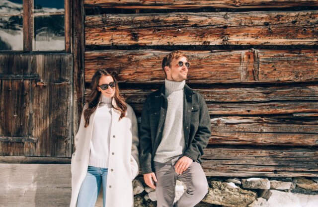 Paar in stylischer Winterkleidung vor einer Holzfassade, ideal für romantische Urlaubsaufnahmen in Lech/Zürs.