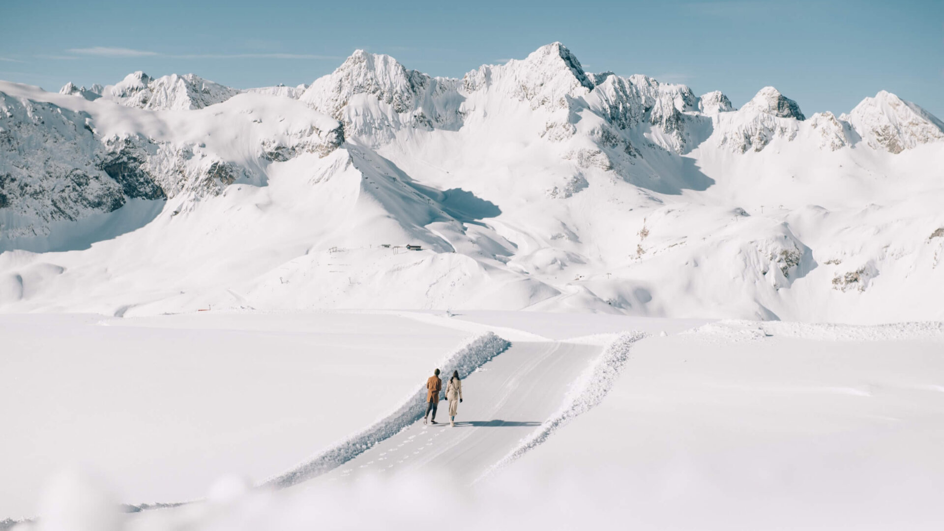 Paar spaziert auf einem schneebedeckten Weg mit beeindruckender Bergkulisse in Lech/Zürs am Arlberg.