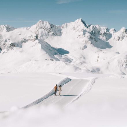 Paar spaziert auf einem schneebedeckten Weg mit beeindruckender Bergkulisse in Lech/Zürs am Arlberg.