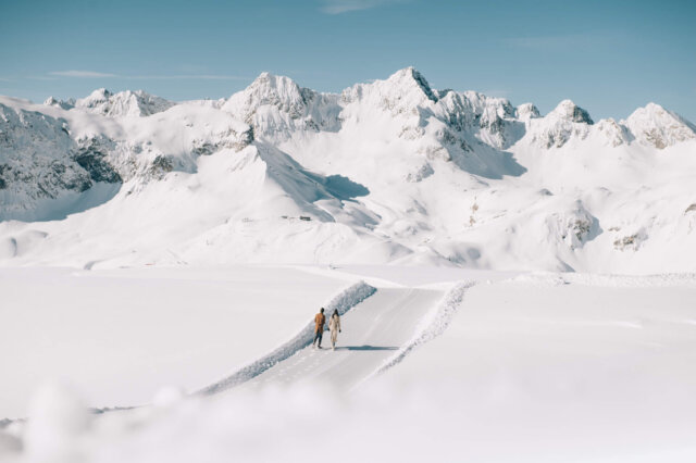 Paar spaziert auf einem schneebedeckten Weg mit beeindruckender Bergkulisse in Lech/Zürs am Arlberg.