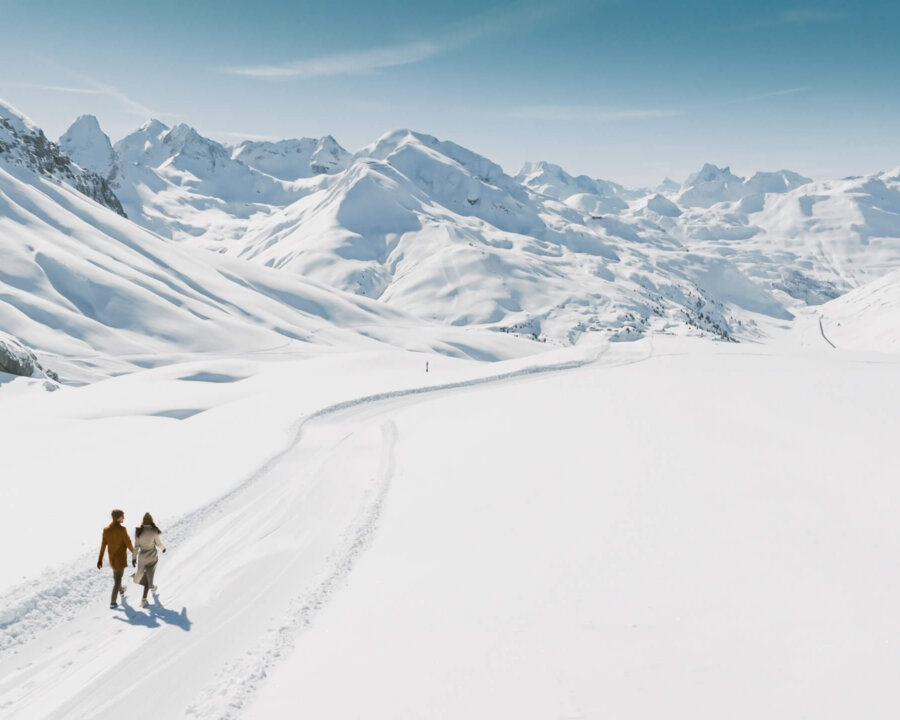 Paar spaziert durch die verschneite Winterlandschaft in Lech/Zürs am Arlberg, umgeben von majestätischen Bergen.