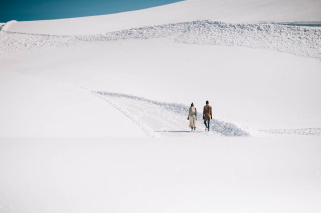 Paar spaziert in der schneebedeckten Landschaft von Lech/Zürs am Arlberg, umgeben von beeindruckender Bergkulisse.