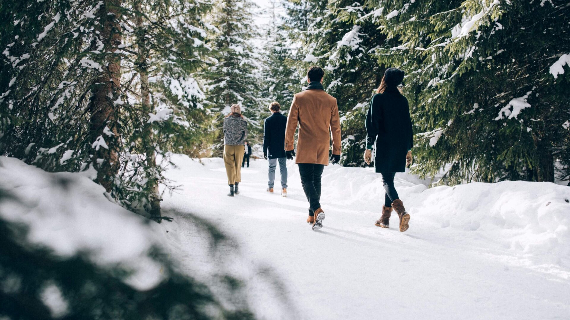 Gruppe von Menschen, die auf einem verschneiten Weg durch fichtenreiche Landschaft in Lech/Zürs spazieren.