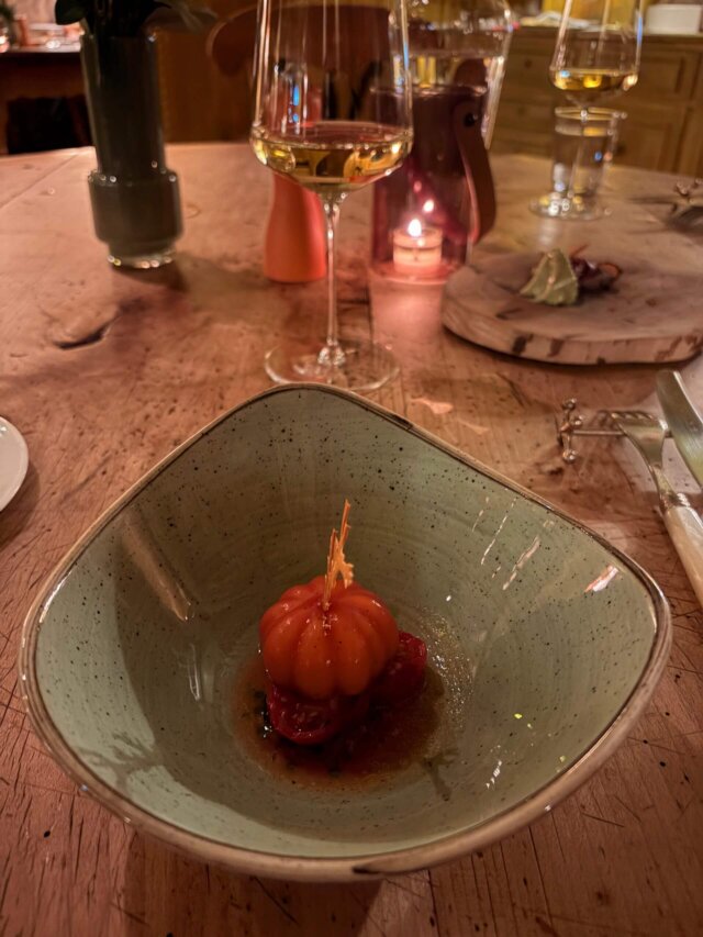 Ein kunstvoll angerichtetes Gericht mit einer orangenen Speise und tomatenähnlichen Zutaten in einem eleganten Restaurant.
