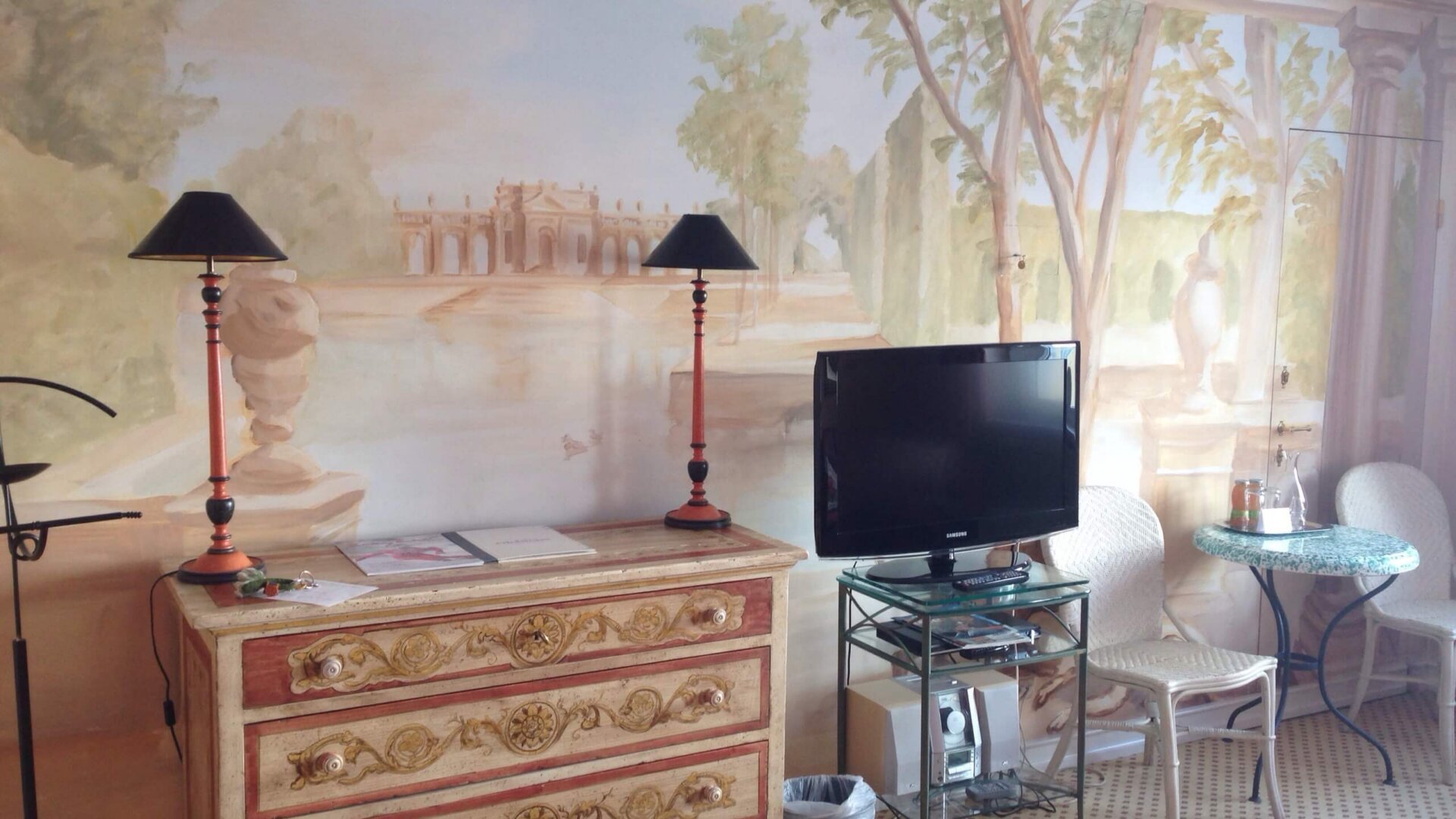 Elegantes Zimmer im Hotel Edelweiss mit kunstvollem Wandgemälde, TV, Stühlen und romantischer Atmosphäre.