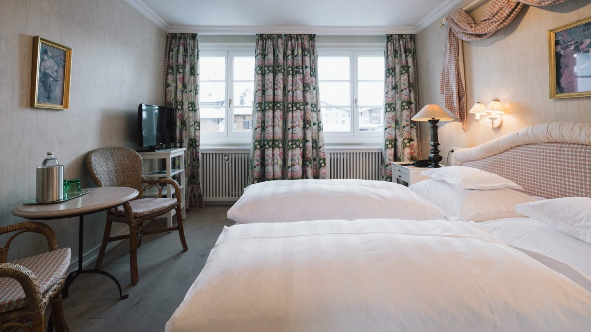 Gemütliches Hotelzimmer im Hotel Edelweiss in Lech/Zürs mit zwei Betten, TV, Tisch und Blick auf die Berge.