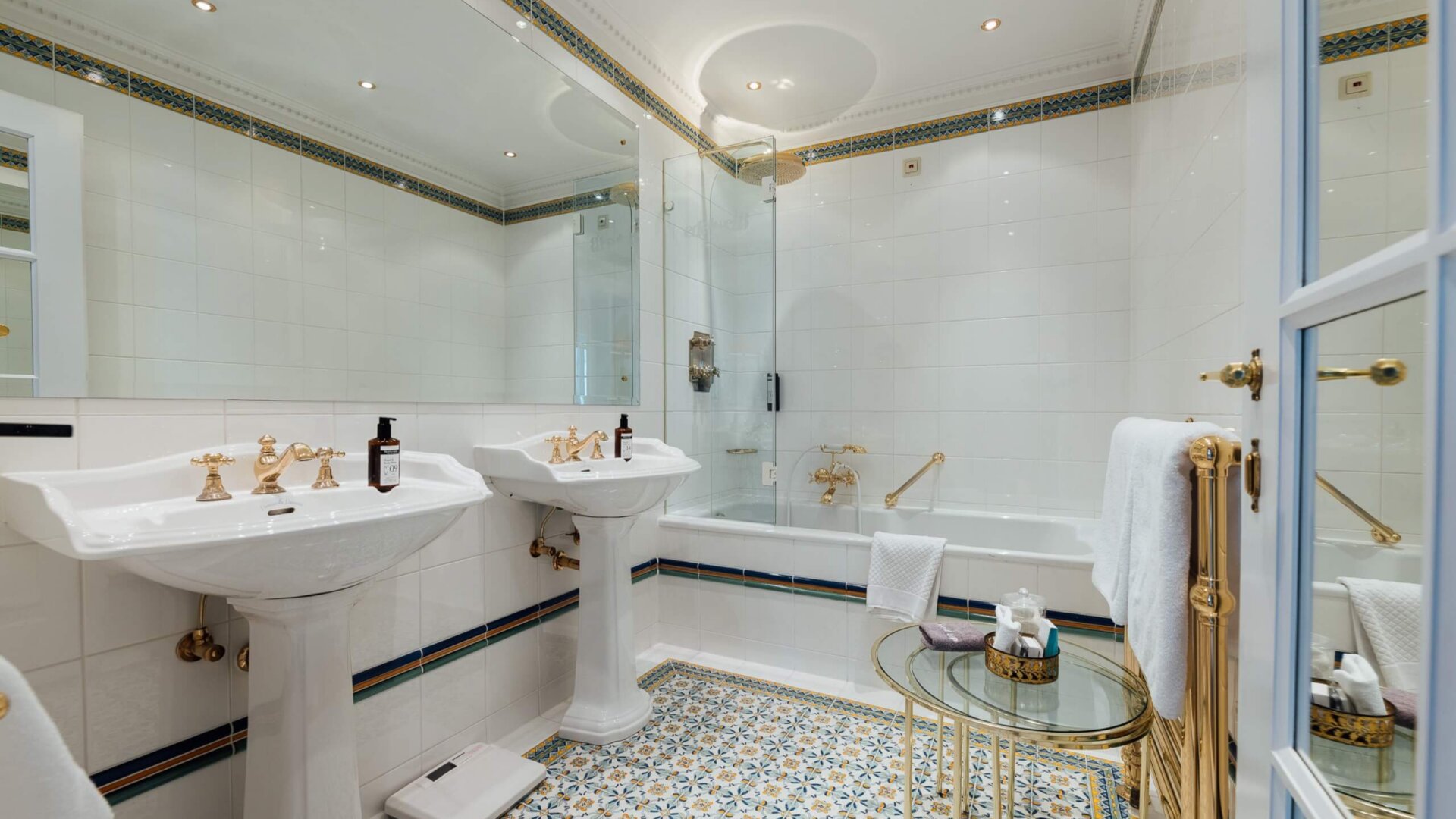 Elegantes Badezimmer im Hotel Edelweiss mit goldenen Armaturen, Mosaikfliesen und luxuriösem Ambiente.