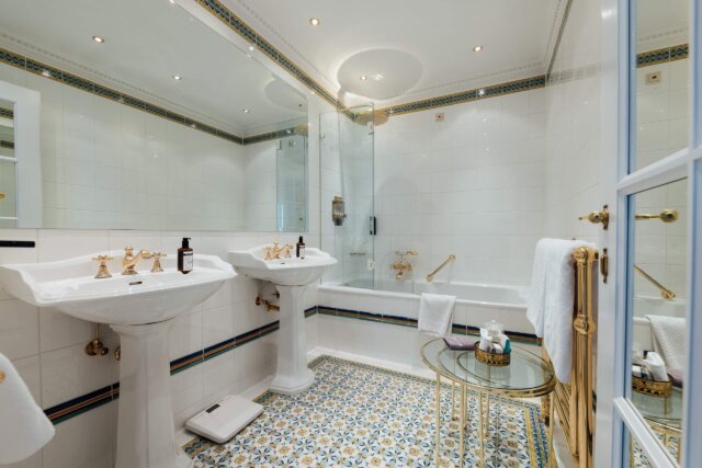 Elegantes Badezimmer im Hotel Edelweiss mit goldenen Armaturen, Mosaikfliesen und luxuriösem Ambiente.