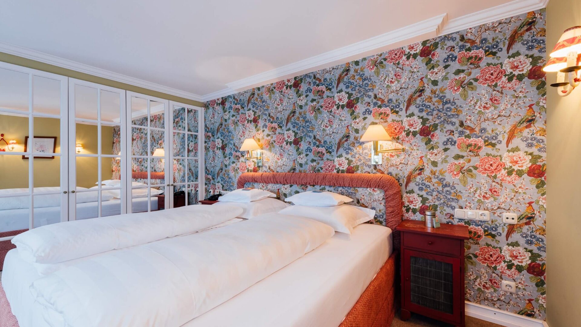 Gemütliches Doppelzimmer im Hotel Edelweiss mit floraler Tapete, gemütlichen Betten und stilvollem Interieur.
