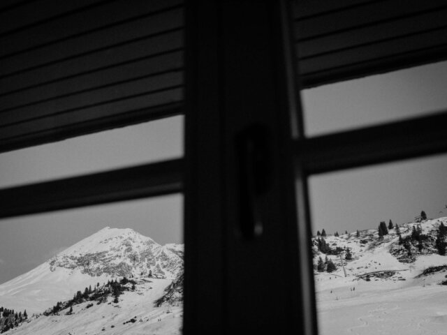 Blick durch ein Fenster auf die verschneiten Berge von Lech/Zürs am Arlberg, ideal für winterliche Erholung.