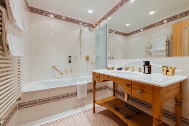 Luxuriöses Badezimmer im Hotel Edelweiss mit Badewanne, eleganten Armaturen und stilvollem Holzwaschtisch.