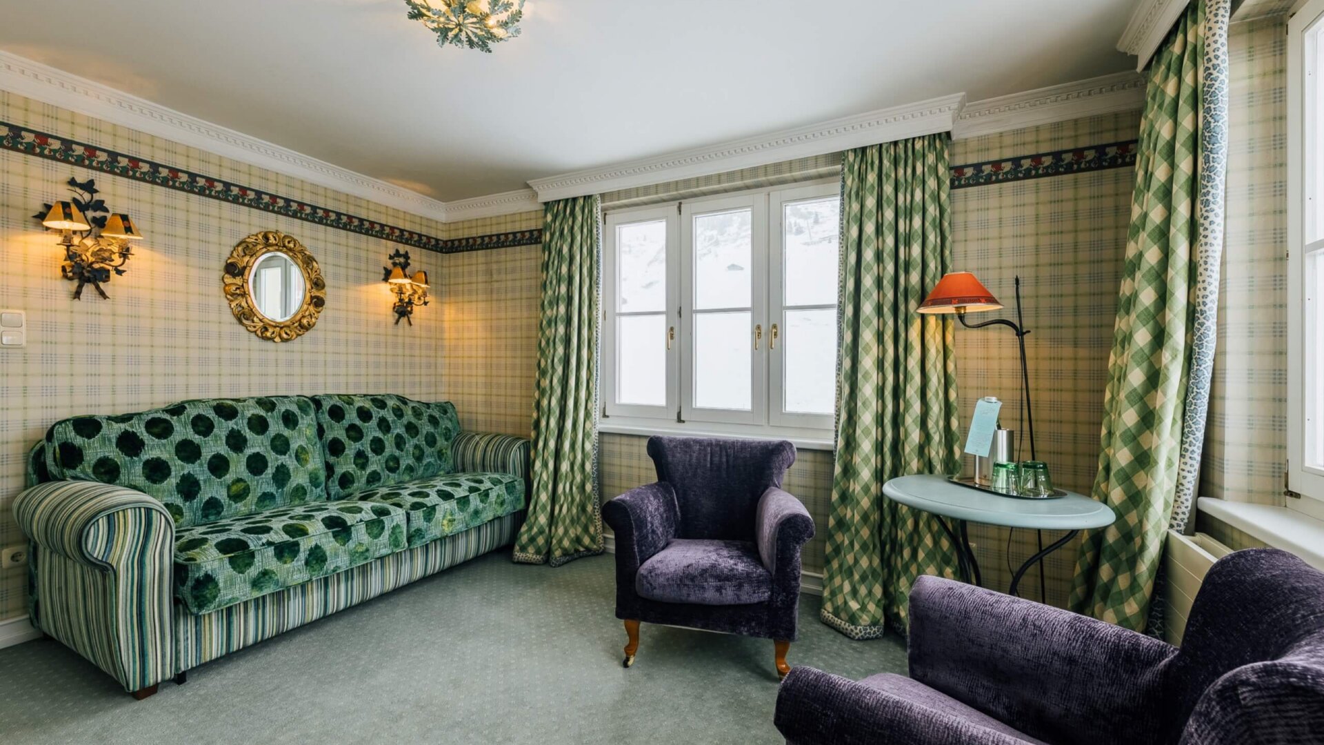 Gemütlicher Hotelzimmer mit grünem Sofa, eleganten Sessel und stilvollen Lampen im Hotel Edelweiss in Lech/Zürs.