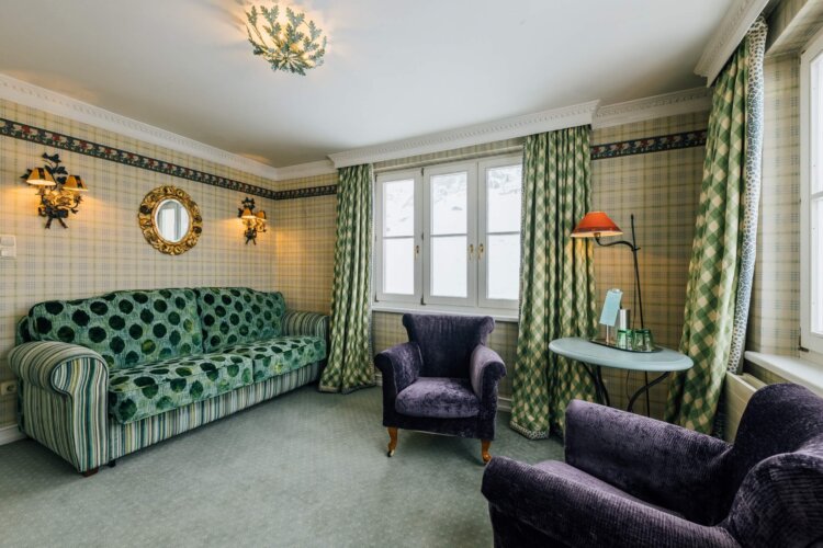 Gemütlicher Hotelzimmer mit grünem Sofa, eleganten Sessel und stilvollen Lampen im Hotel Edelweiss in Lech/Zürs.