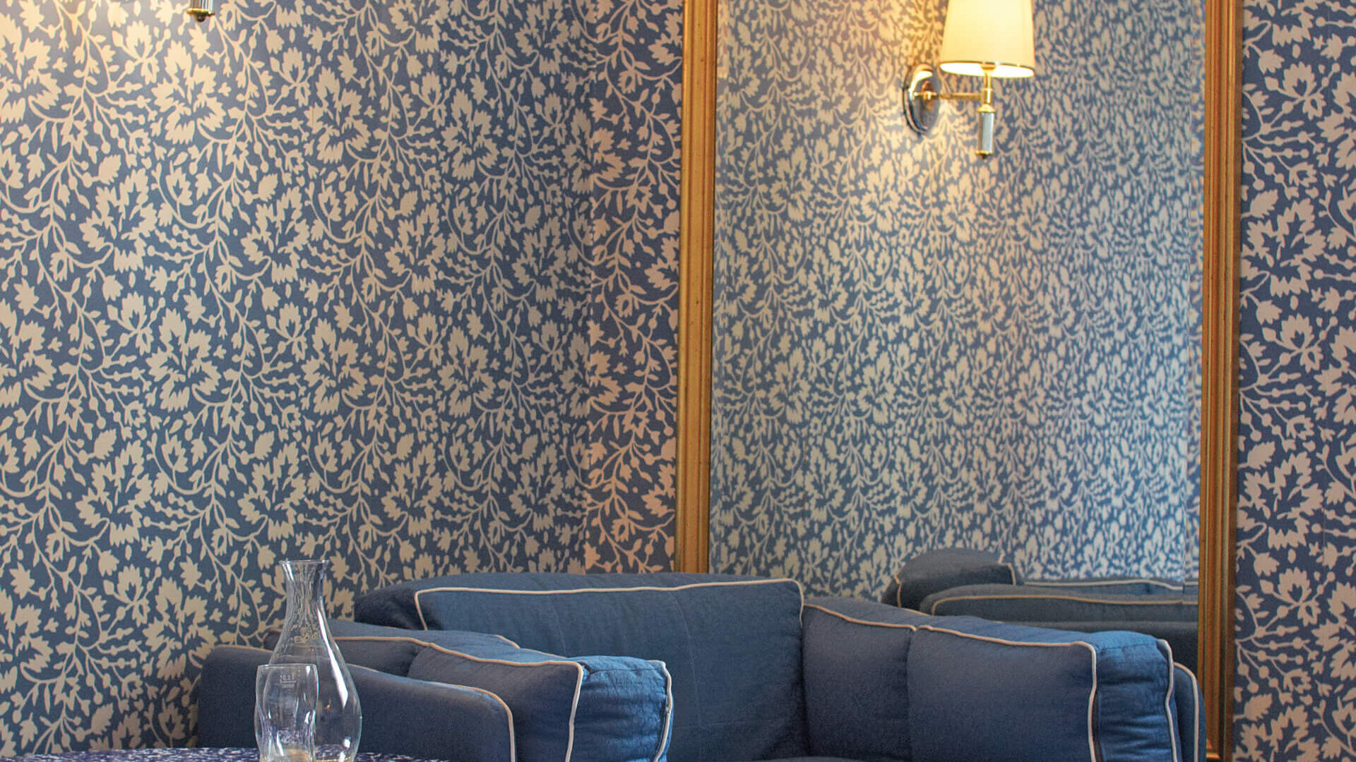Gemütliche Ecke im Hotel Edelweiss mit blauem Sessel, dekorativer Tapete und elegantem Spiegel.