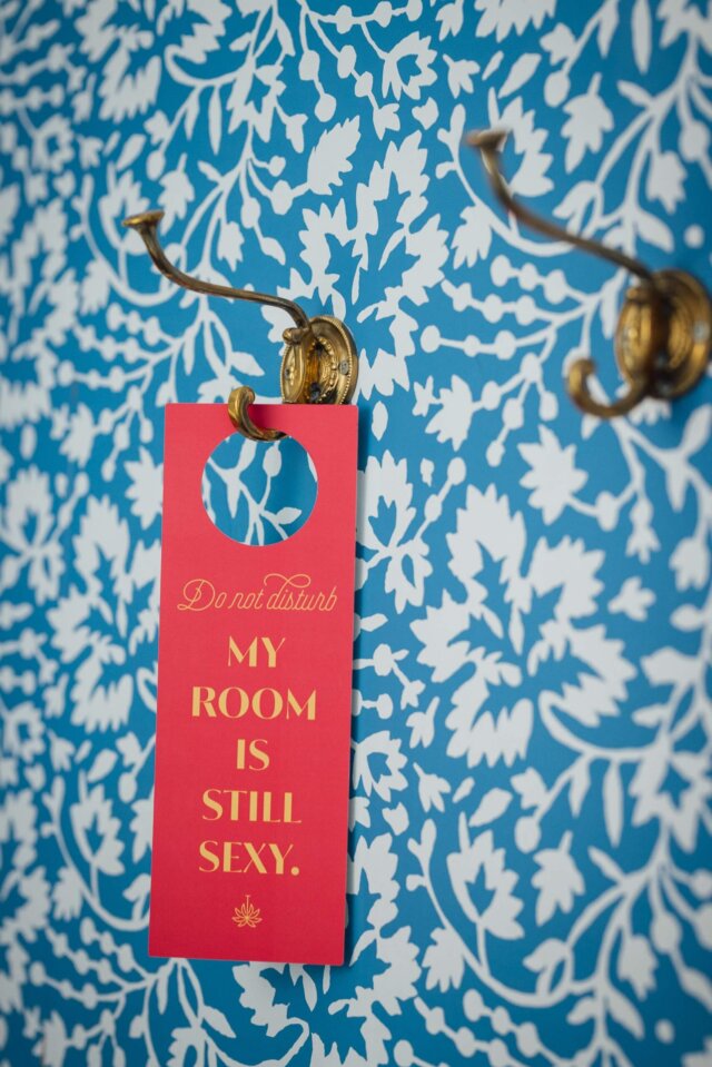 Rotes „Do not disturb“-Schild hängt an goldenen Haken vor einem blauen, floral gemusterten Hintergrund im Hotel Edelweiss.