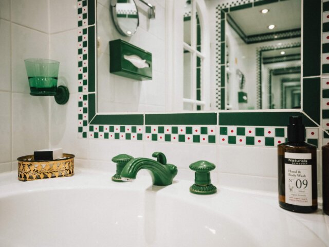 Elegantes Bad mit grünen Armaturen, stilvollem Spiegel und luxuriösen Pflegeprodukten im Hotel Edelweiss in Lech/Zürs.