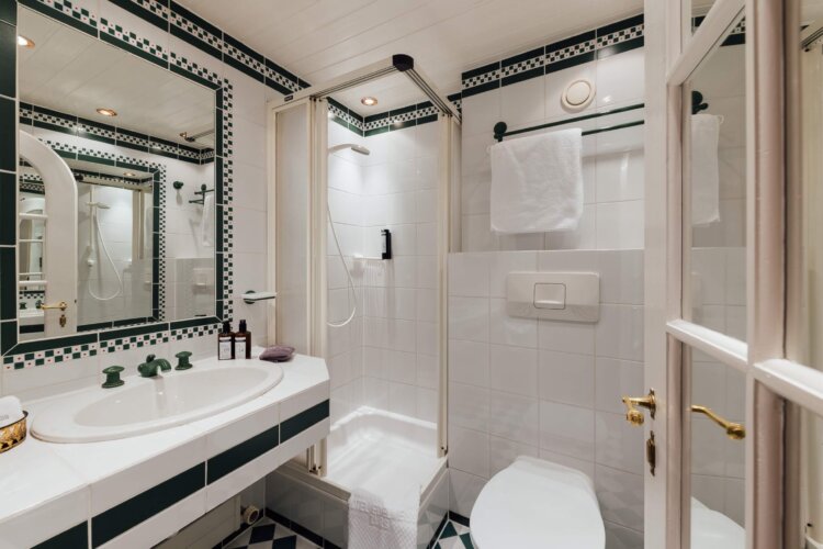 Elegantes Badezimmer im Hotel Edelweiss in Lech/Zürs mit Dusche, Waschbecken und stilvollen Fliesen.
