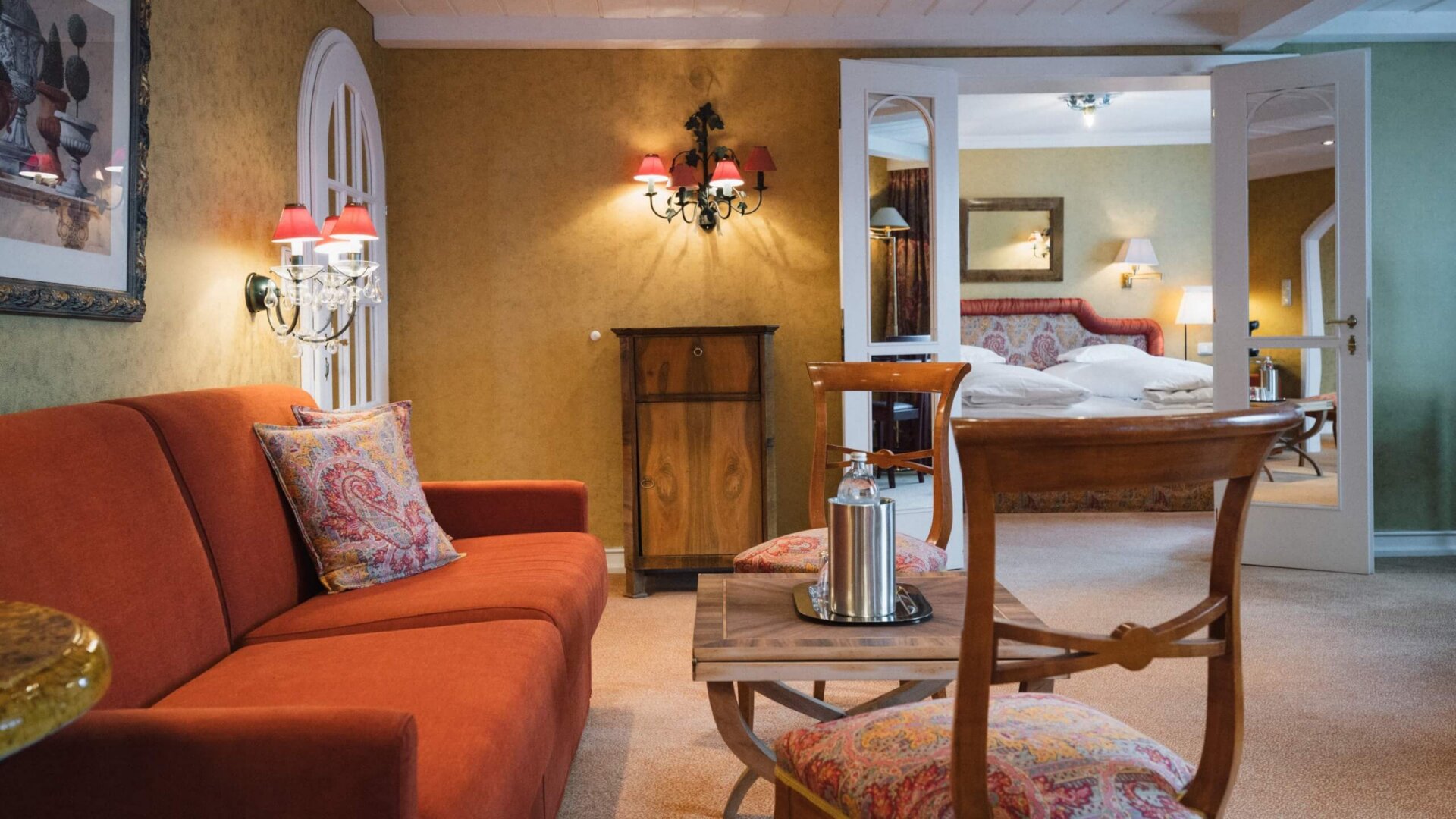 Gemütliche Suite im Hotel Edelweiss mit rotem Sofa, eleganten Details und Zugang zum Schlafzimmer in Lech/Zürs.