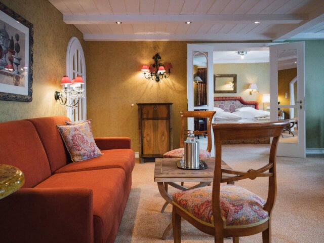 Gemütliche Suite im Hotel Edelweiss mit rotem Sofa, eleganten Details und Zugang zum Schlafzimmer in Lech/Zürs.