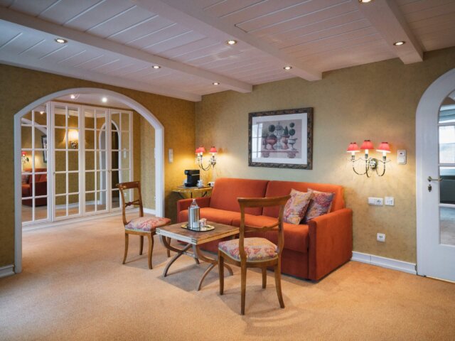 Gemütlicher Wohnbereich im Hotel Edelweiss, Lech/Zürs, mit einem orangefarbenen Sofa, dekorativen Leuchten und stilvollem Ambiente.