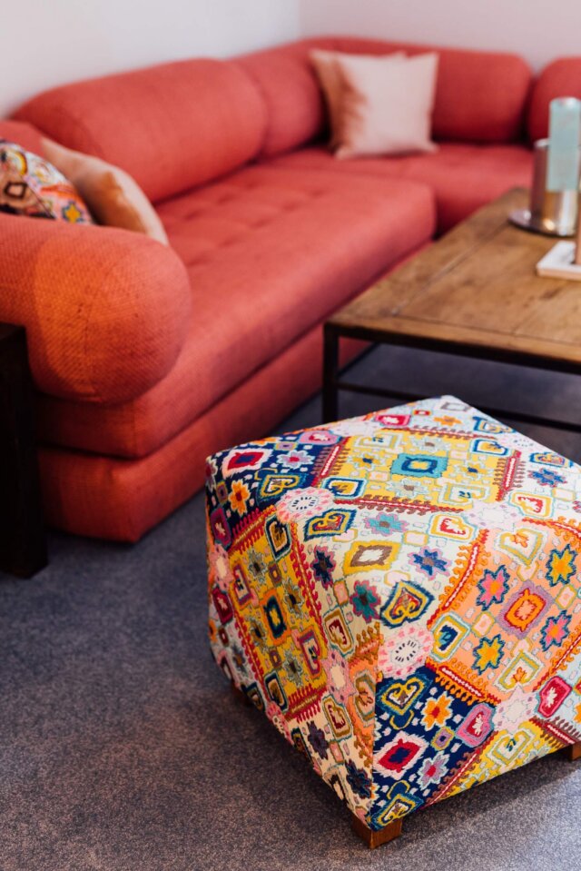 Bequeme Wohnatmosphäre im Hotel Edelweiss: stylisches Sofa und bunter Pouf im gemütlichen Aufenthaltsraum.
