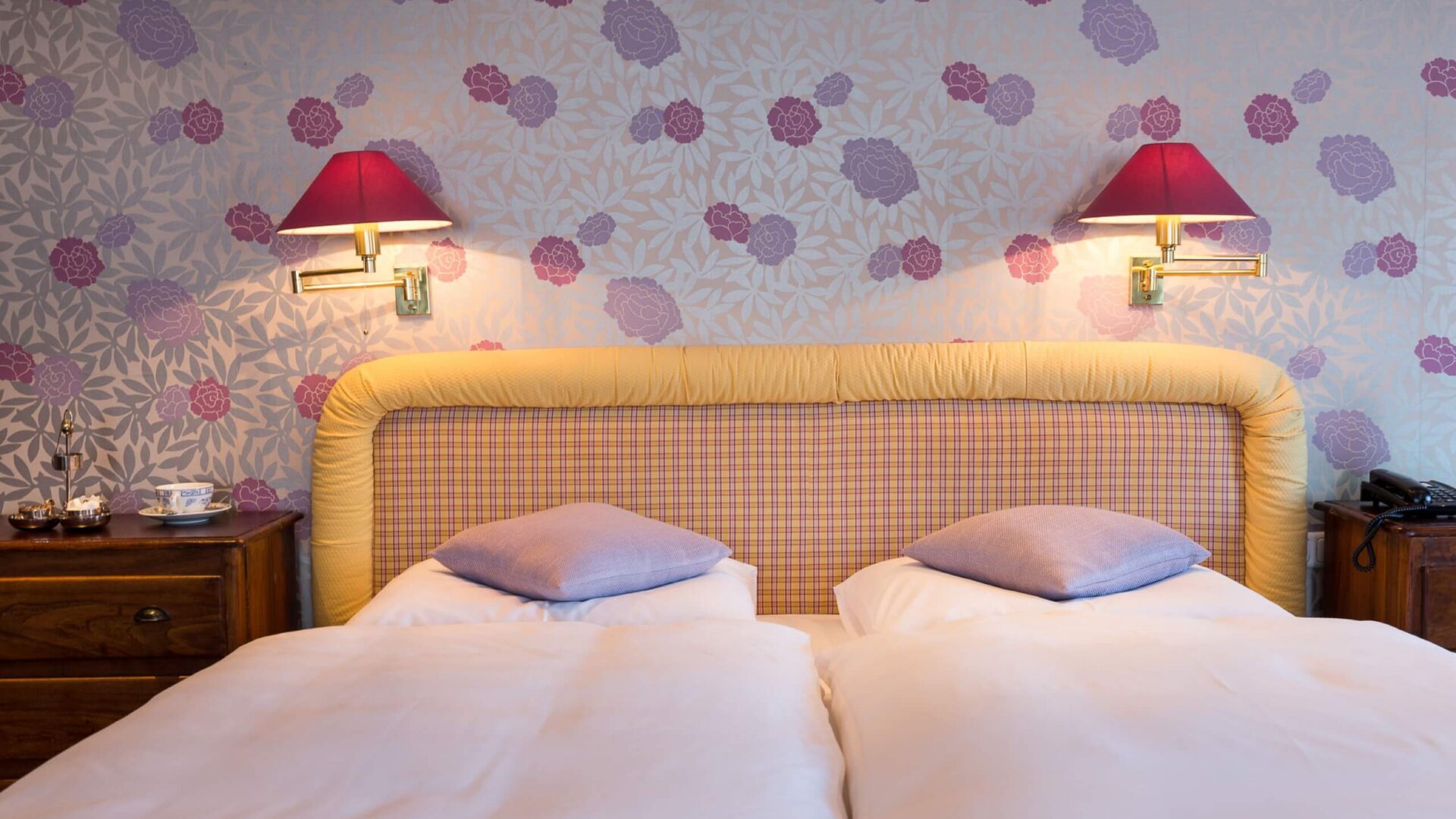 Gemütliches Hotelzimmer im Hotel Edelweiss in Lech/Zürs, mit blumigem Tapetenmuster und stilvollen Beleuchtungselementen.