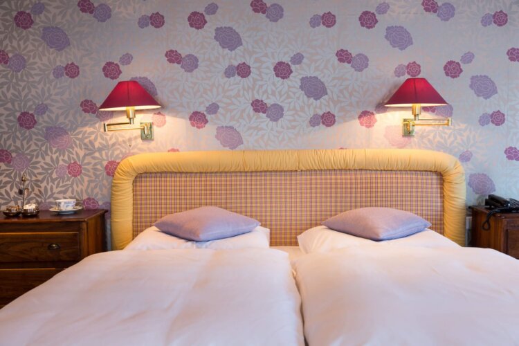 Gemütliches Hotelzimmer im Hotel Edelweiss in Lech/Zürs, mit blumigem Tapetenmuster und stilvollen Beleuchtungselementen.