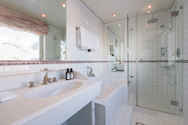 Modernes Badezimmer im Hotel Edelweiss mit eleganter Badewanne, Regendusche und stilvollen Accessoires.