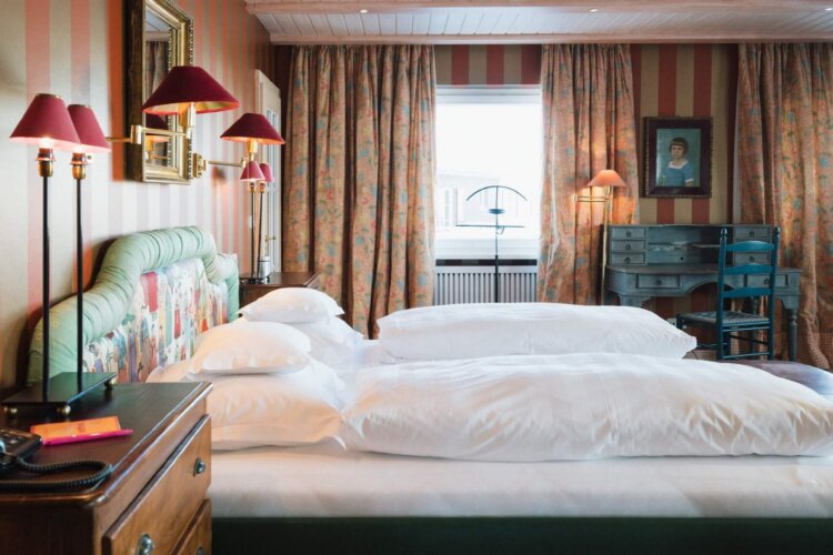 Gemütliches Zimmer im Hotel Edelweiss, Lech/Zürs: stilvolle Einrichtung mit bunten Vorhängen und einem gemütlichen Bett.