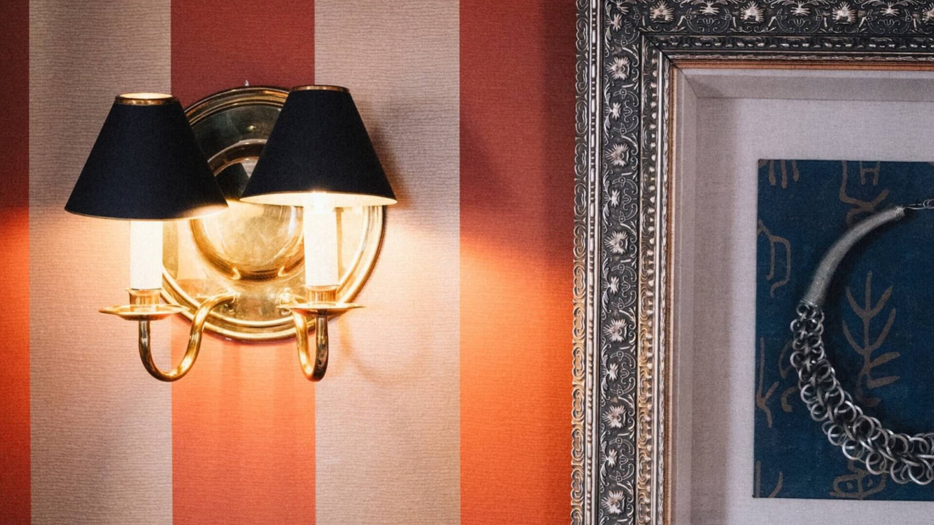 Gemütliche Hotelzimmeratmosphäre im Hotel Edelweiss: elegante Wandleuchte und stilvolles Kunstwerk an rot gestreiften Wänden.