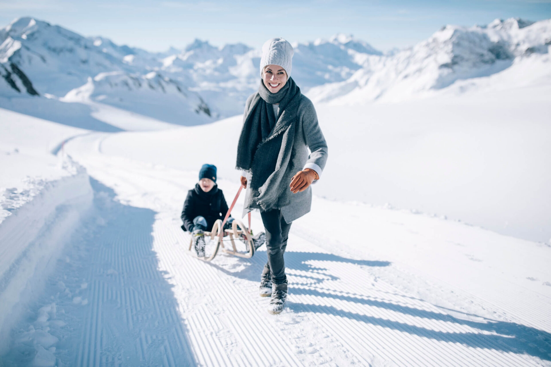 Frau zieht im Schnee einen Schlitten mit einem Kind, umgeben von wunderschöner Winterlandschaft in Lech/Zürs.