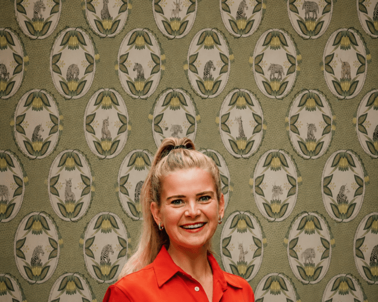 Lächelnde Frau in rotem Outfit vor einem bunten Muster; Foto für die Website des Hotels Edelweiss in Lech/Zürs.