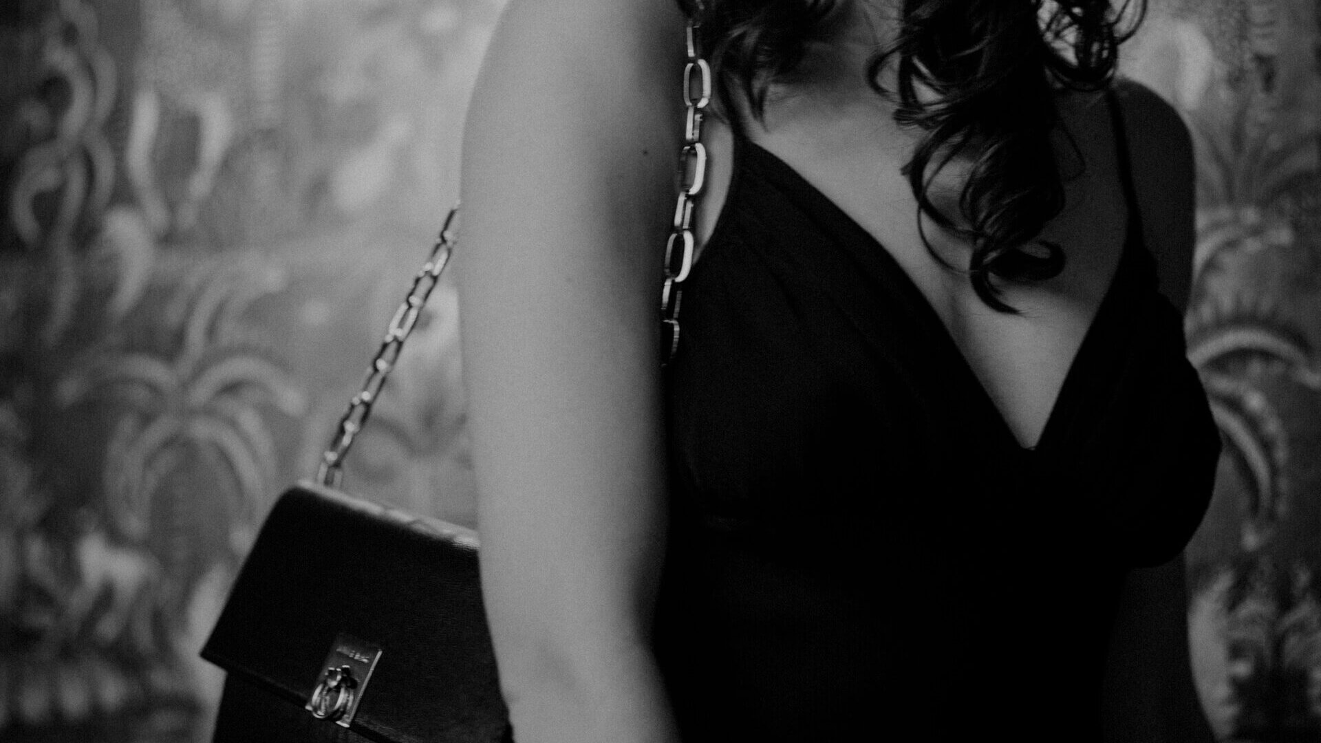 Elegante Frau in schwarzem Kleid mit Handtasche, dekorativer Hintergrund im Hotel Edelweiss in Lech/Zürs.